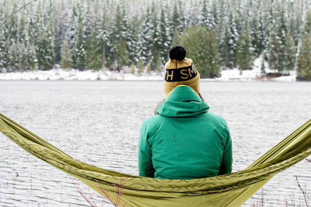 Sitting lakeside in a hammock, embracing winter and taking in the snowy view.