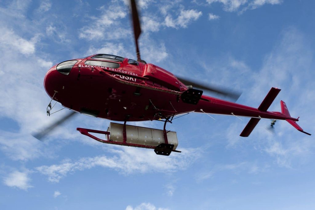 The iconic red Blackcomb helicopter makes its ways across a blue sky.