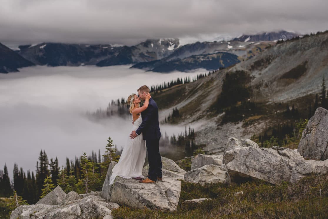 A bride and groom lovingly embrace atop the mountains in Whistler.