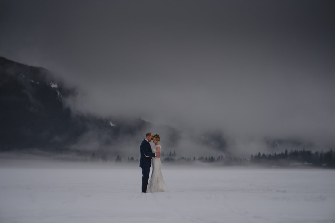 A bride and groom embrace in snowy surroundings.